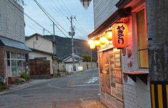 暮れかけた赤湯の路地。軒先にやきとりの赤提灯が灯り、道の先に山並みが見える　／　00_eyecatch_yakitori_chochin.jpg