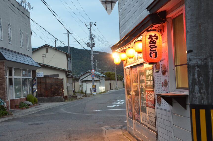 暮れかけた赤湯の路地。軒先にやきとりの赤提灯が灯り、道の先に山並みが見える　／　00_eyecatch_yakitori_chochin.jpg