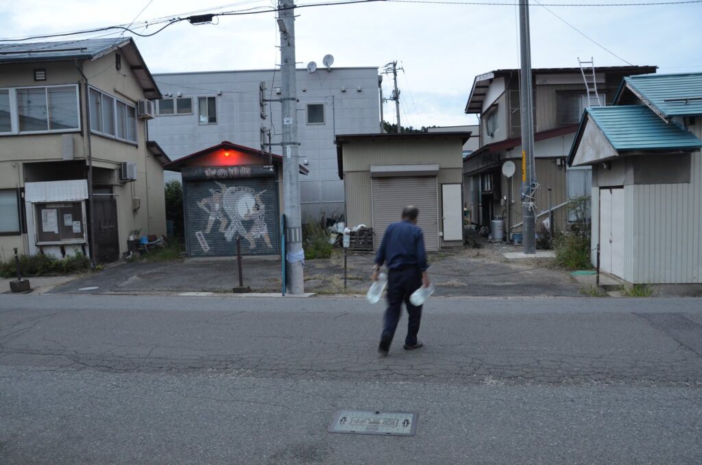 両手にペットボトルを提げ、通りを渡っていく人の後ろ姿　／　07_petbottle_onsensui.jpg